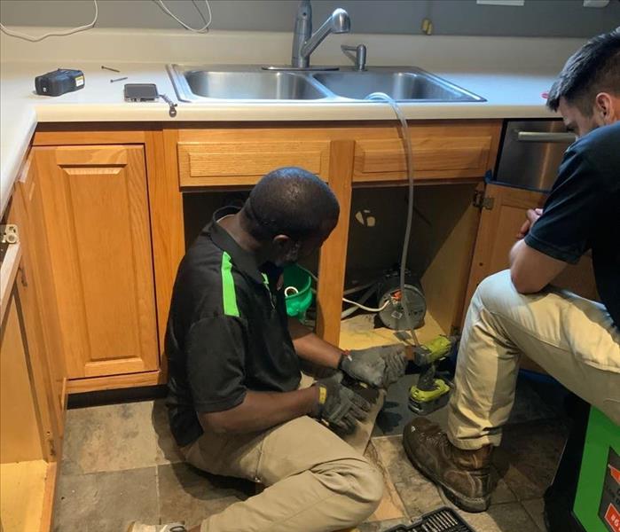 two servpro workers working underneath a sink 