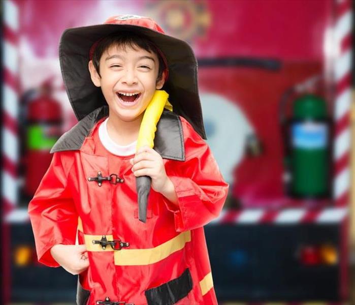 Little boy dressed as a firefighter and holding a hose over his shoulder
