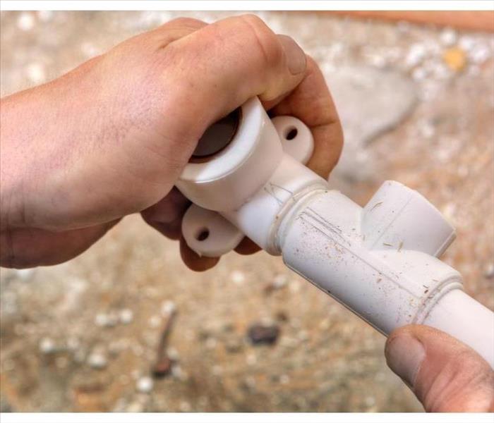 The plumber connects parts of the plastic water pipe using fittings, hands close-up.