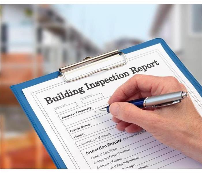 Writing on a clipboard to a paper that says Building Inspection